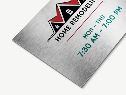 Brushed aluminum business sign with home remodeling logo featuring red and black rooftops, displaying business hours Monday to Thursday from 7:30 AM to 7:00 PM.