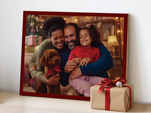 Wooden photo sign showing a smiling family and their dog during Christmas, placed beside a wrapped gift box.