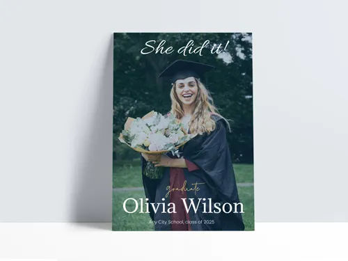 Graduation signage with smiling graduate holding bouquet in cap and gown on green background