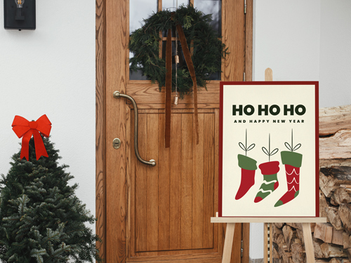 Ho Ho Ho Christmas foam board sign with festive stockings displayed on an easel outside a decorated wooden door.