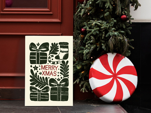 Merry Xmas gatorboard sign featuring hand-drawn gifts and holiday elements placed beside a Christmas tree and large candy décor.