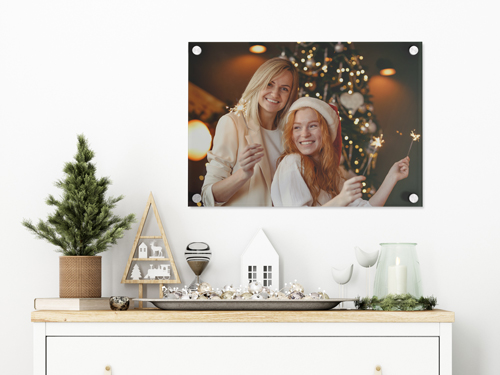 Acrylic photo print of two women celebrating Christmas with sparklers, displayed on a holiday-decorated shelf.
