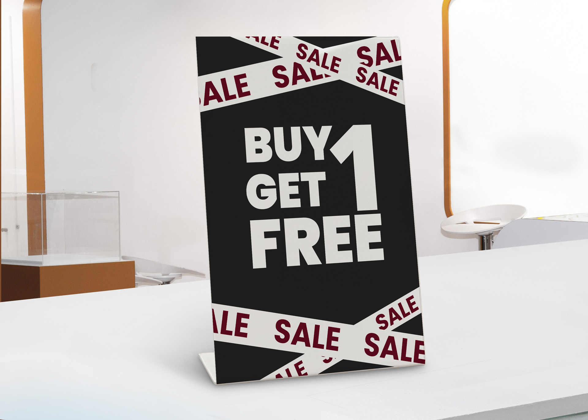 Buy 1 Get 1 Free promotional pedestal sign with sale tape on white surface.