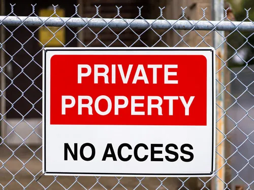 Private property aluminum sign with bold red and white design, mounted on a chain-link fence for clear no access warning.