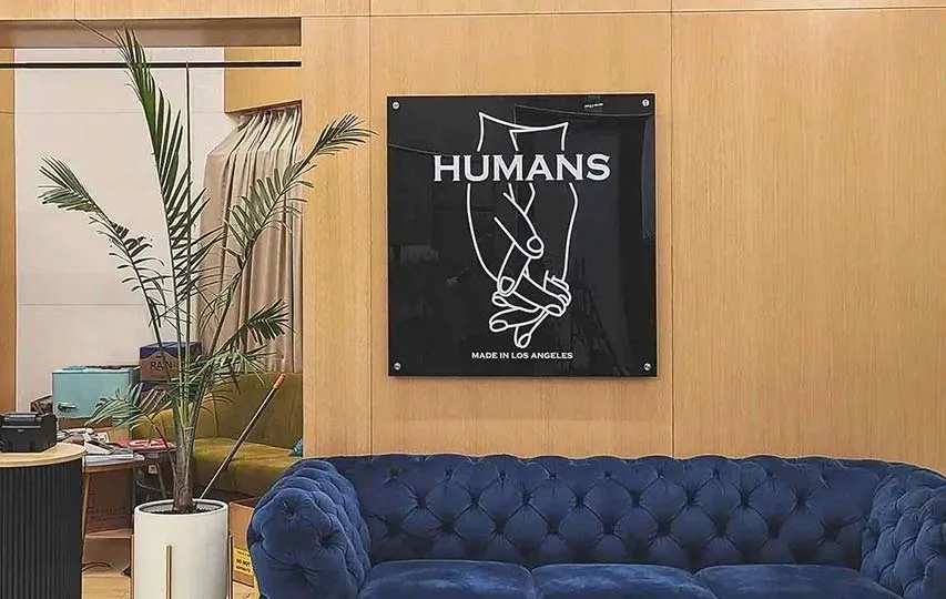 A black acrylic sign mounted on a wooden wall depicting two hands with intertwined fingers and the word Humans.
