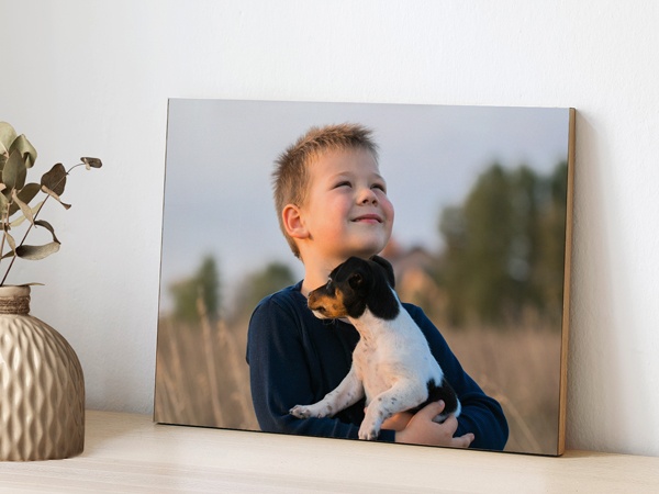 Wooden photo print of a young boy holding a small dog outdoors, displayed on a tabletop next to home décor.